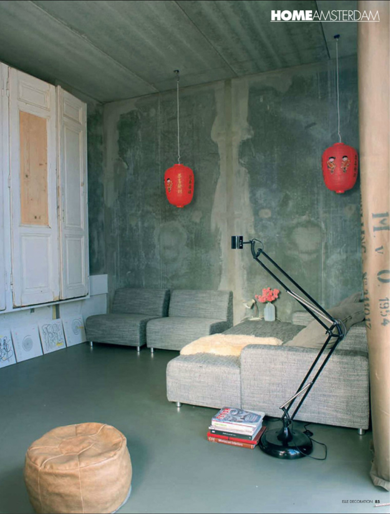 Un salon aux murs en béton brut avec du mobilier design et une armoire de brocante