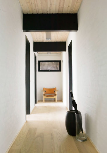 Un couloir minimaliste avec un parquet en bois, murs blancs soulignées d'encadrements de porte peints en noir