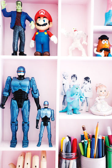 Collection de figures de super héros, exposées dans une bibliothèque rose bonbon