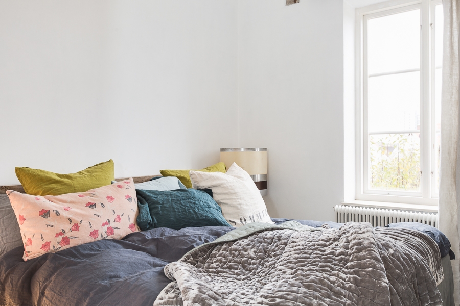 Un lit avec du linge de maison dépareillé pour une chambre blanche minimaliste