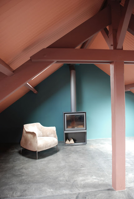 Une charpente de toit, peinte en rouille avec un mur gris turquoise et un sol en béton ciré gris. Il fallait oser