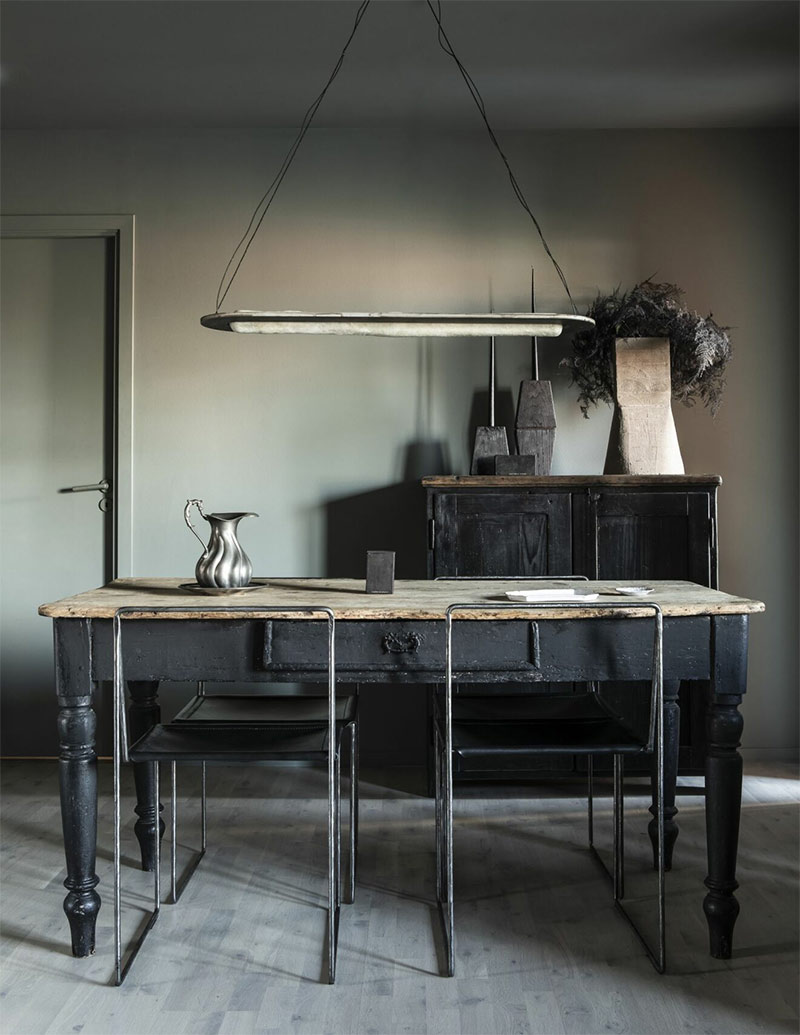 Une salle à manger de style industriel avec une vieille table de tapissier patinée et des objets design en métal Une salle à manger de style industriel avec une vieille table de tapissier patinée et des objets design en métal