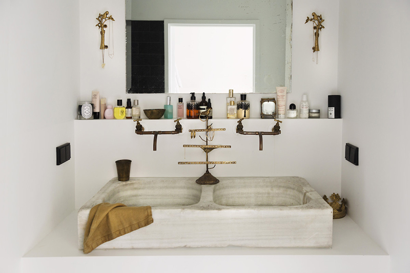 Petit coin lavabo mis en scène avec une collection de produits de beauté et de parfums