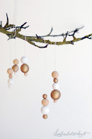 Ensemble de boules de Noël blanches, dorées et en bois naturel suspendues à une branche Ensemble de boules de Noël blanches, dorées et en bois naturel suspendues à une branche