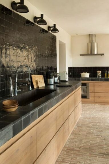 Une cuisine bois avec une crédence en zellige noir et plan de travail noir par Hanne Benoist interieur