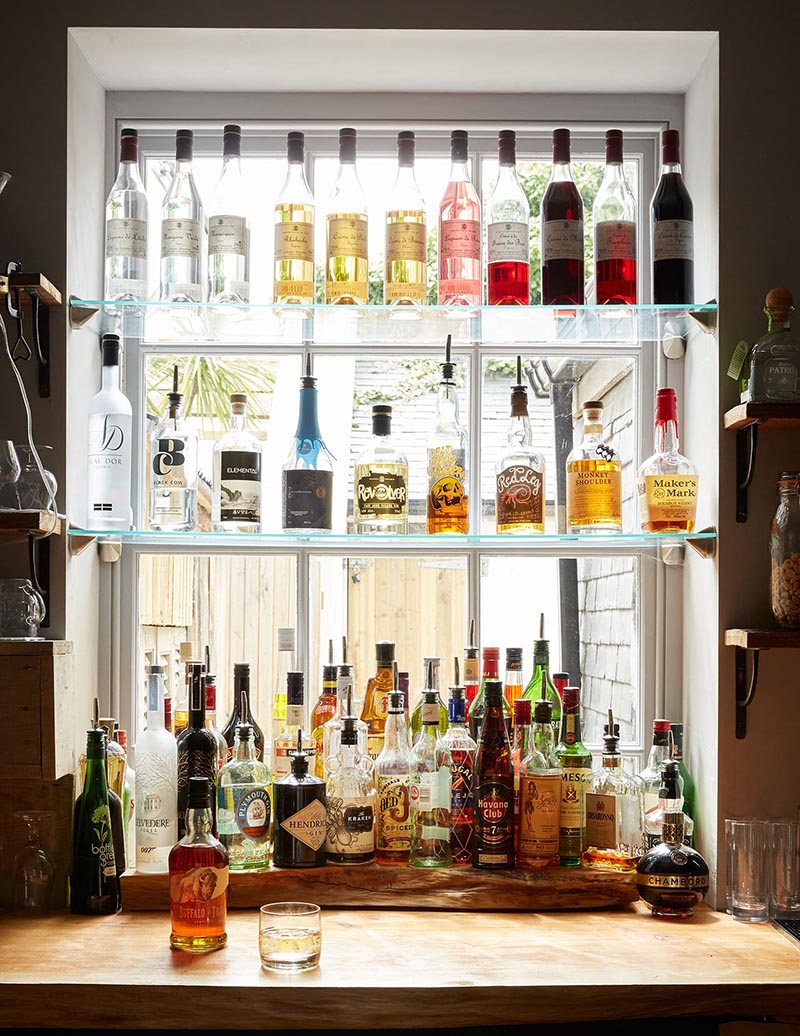 Des étagères murales en verre installées devant une fenêtre pour faire un bar à cocktail
