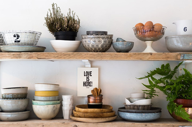 Les étagères de cuisine en bois brut sur lesquelles sont disposées de la jolie vaisselle en céramique Les étagères de cuisine en bois brut sur lesquelles sont disposées de la jolie vaisselle en céramique