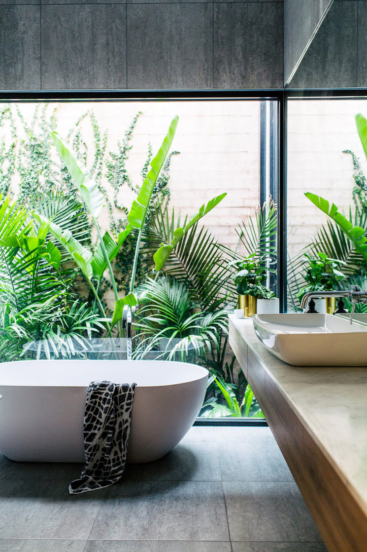 Salle de bains avec baignoire îlot avec une baie vitrée donnant sur un patio