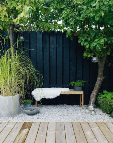 Une palissade peinte en noir, quelques pots, un banc en bois et des graviers