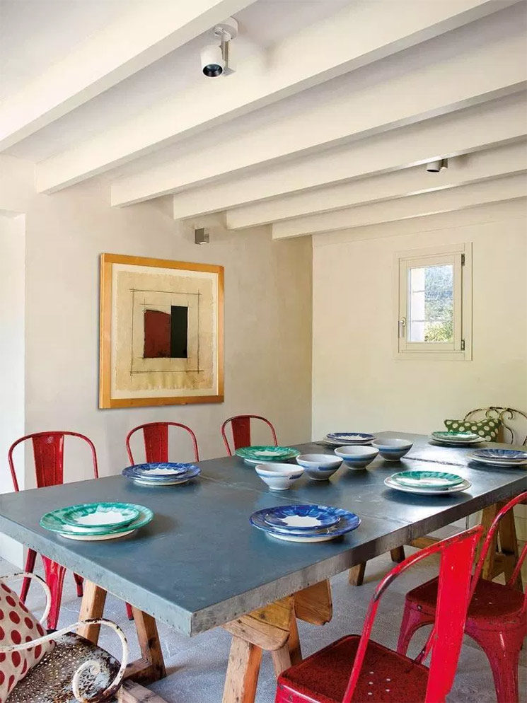 Une table de salle à manger en métal posée sur tréteaux avec des chaises Tolix rouge