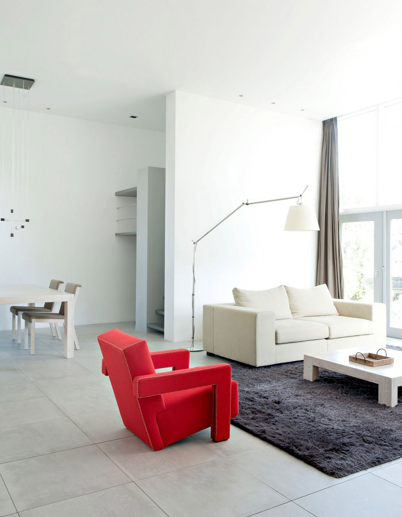 Un séjour blanc monochrome, révaillé par un fauteuil rouge et un tapis anthracite