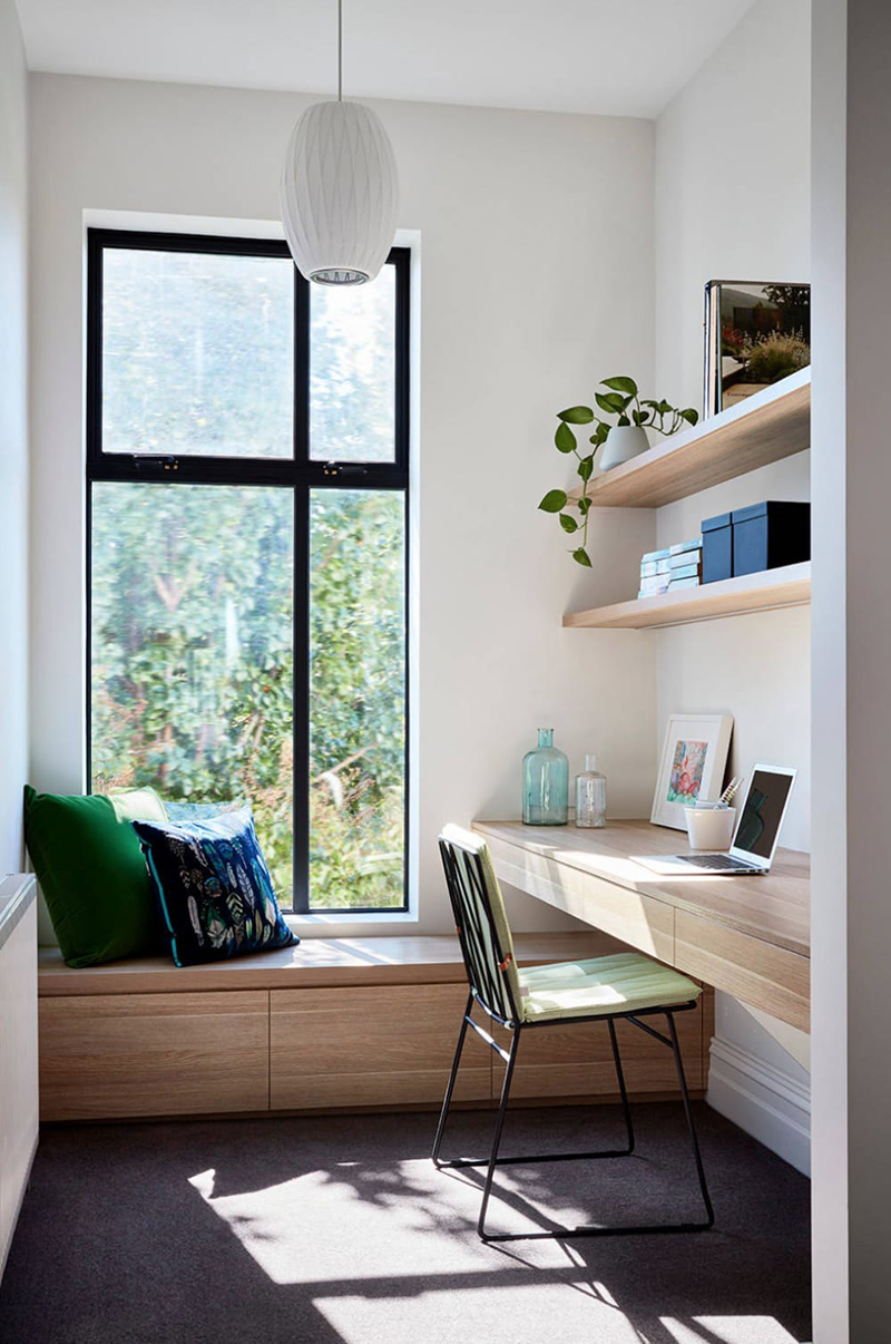 Un petit bureau aménagé dans une petite pièce avec son banc en dessous de la fenêtre