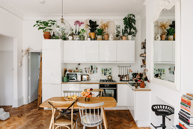 Cuisine laquée blanche, en L, avec une série de plantes placées au dessus des placards