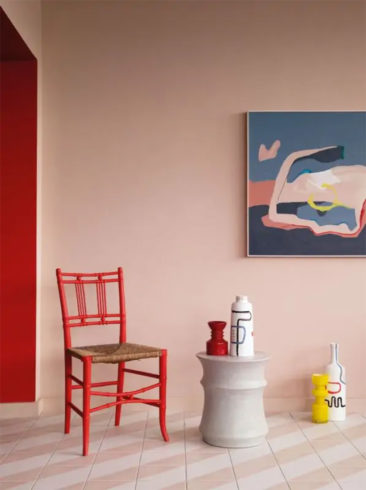 Une chaise rouge vermillon, dont le rouge est atténué par le mur rose claire