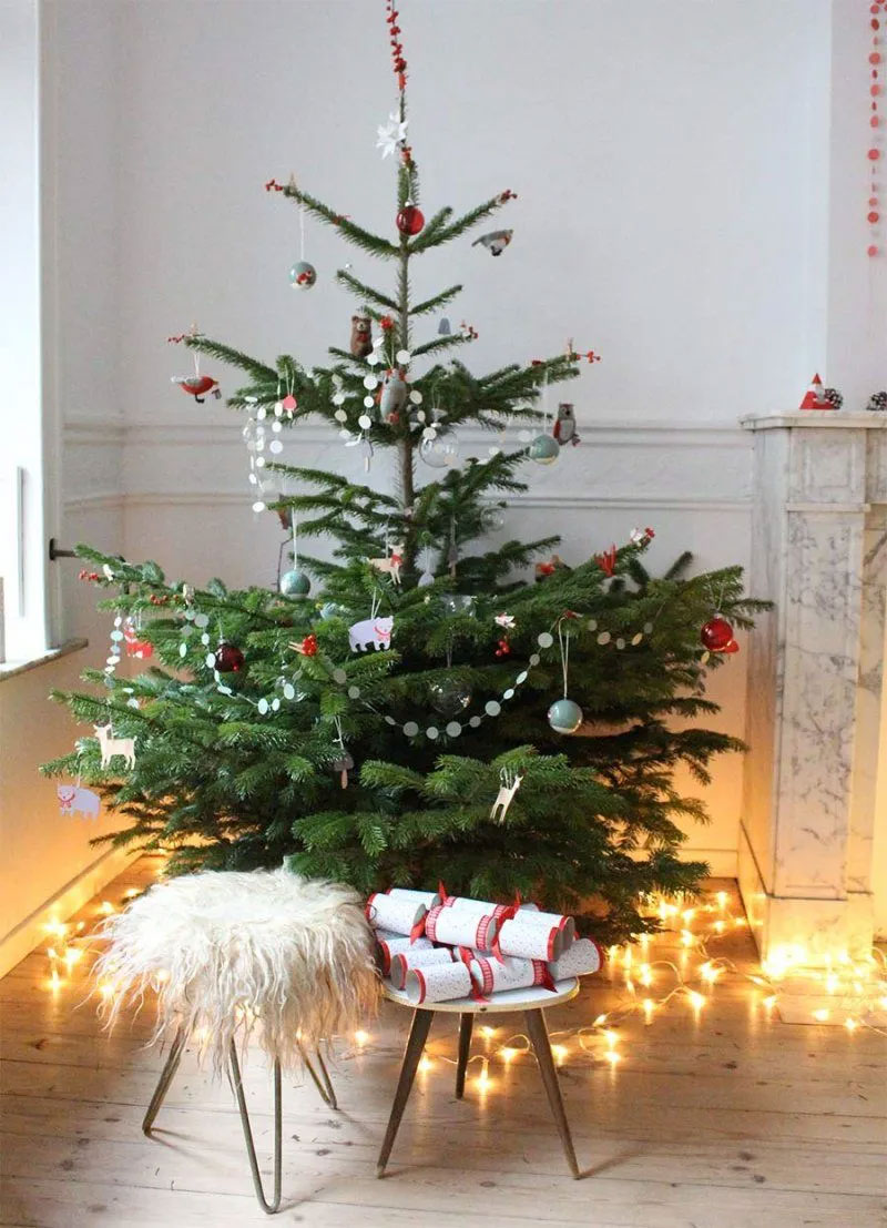 Un sapin de Noël joliment décoré avec sa guirlande électrique placé à son pied