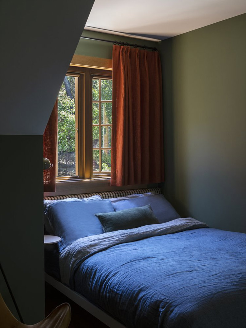 Une petit chambre verte aux rideaux rouges sous les combles avec du linge de lit bleu