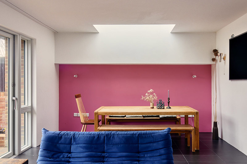 Un mur en rose vif peint au fond du séjour pour encadrer le coin repas