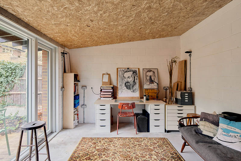 Une pièce atelier blanche, ouverte sur le jardin par une grande baie vitrée. La caractéristique sont plafond en OSB.