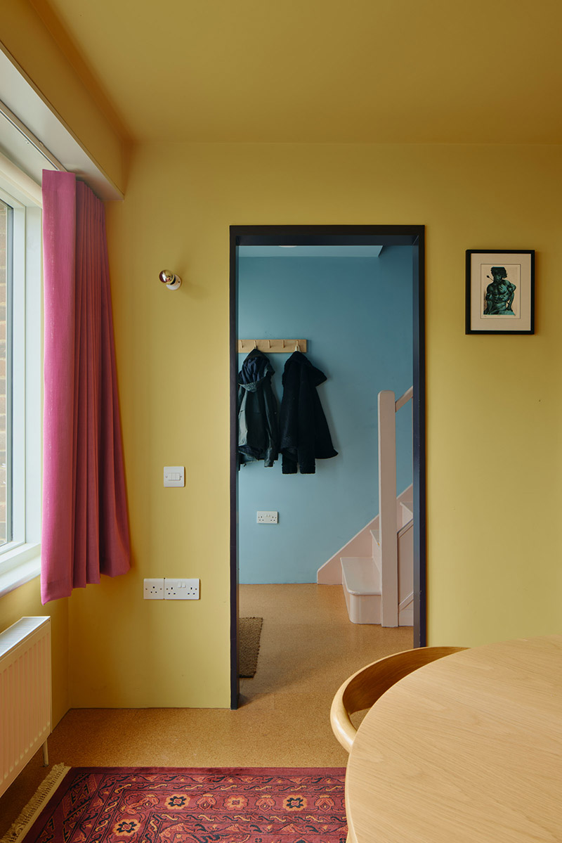 La salle à manger jaune ocre donne sur le couloir bleu avec un encadrement de porte noir