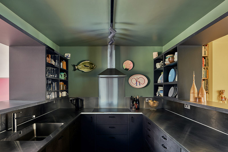 Une cuisine en mode color block avec des placards noirs et des murs vert olive