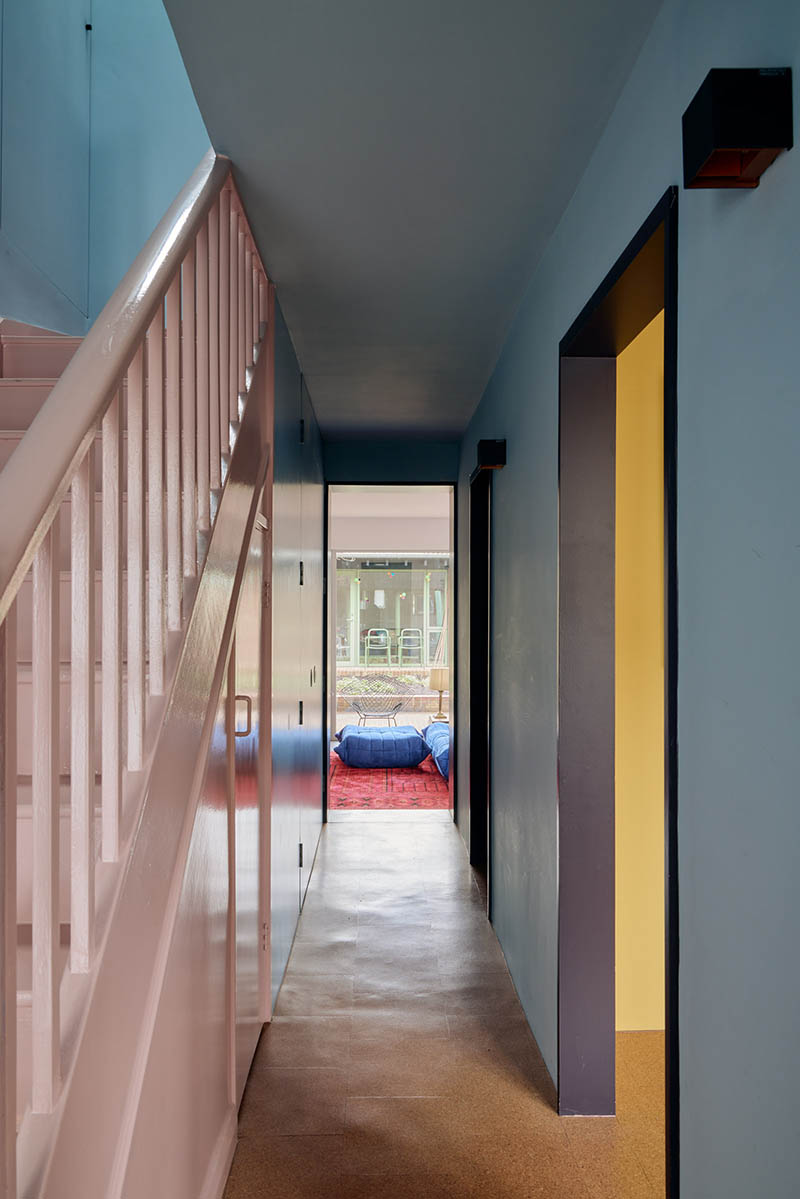 Une couloir en mode color block avec un escalier peint en rose et des murs bleus