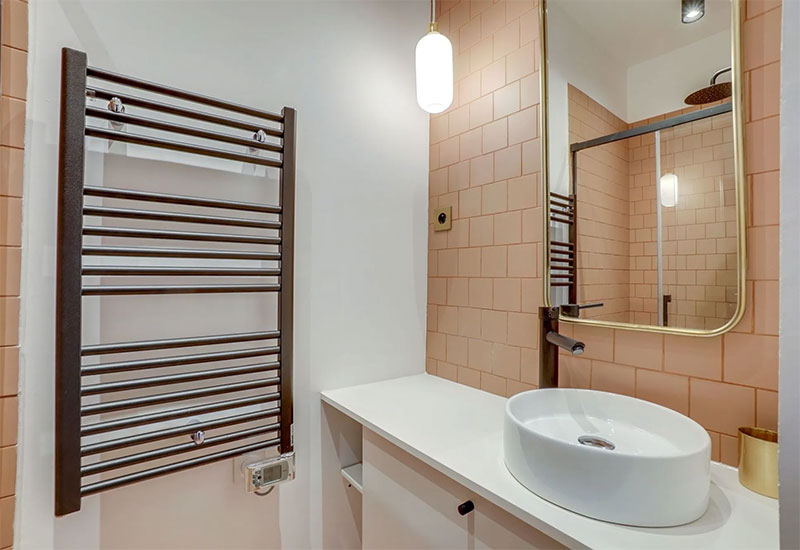 Salle de bains équipée d'un sèche serviette noir sur mur blanc et carrelage abricot