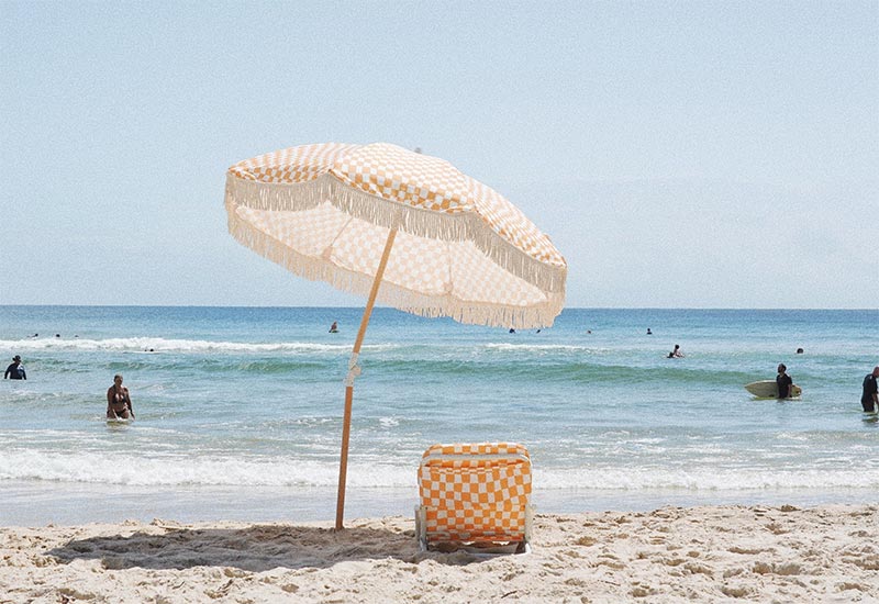 Parasol à damier orange et blanc sur une plage paradisiaque - Catalogue Sunday Supply