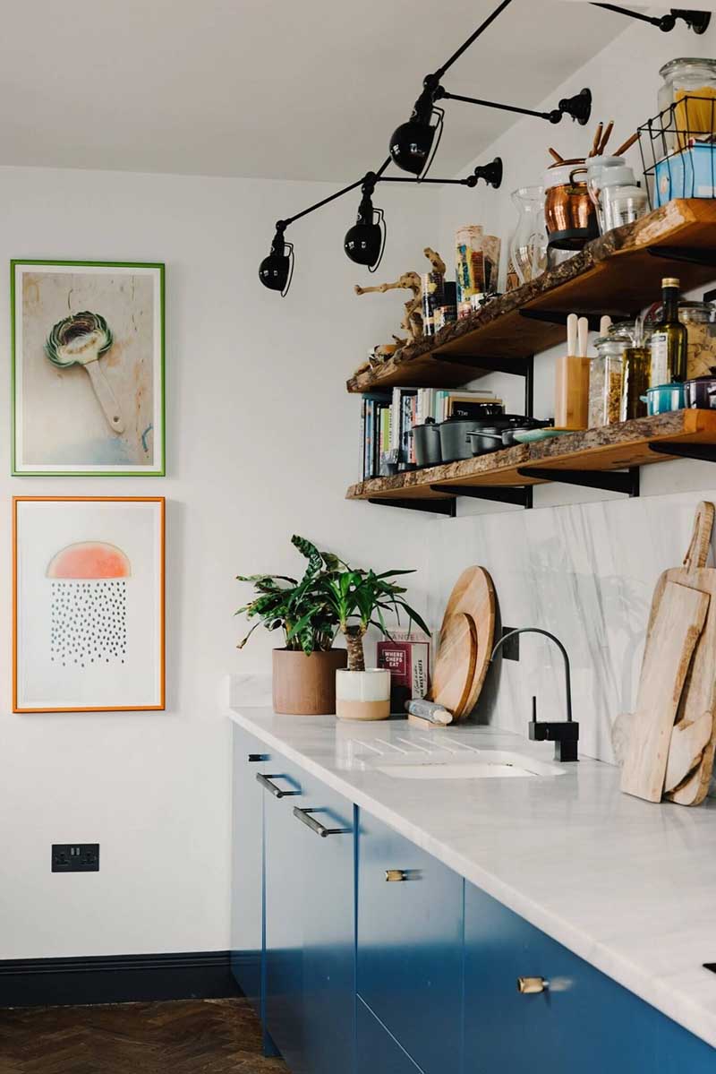 Une cuisine bleue avec des étagères de cuisine en bois brut et des appliques murales Jielde noires