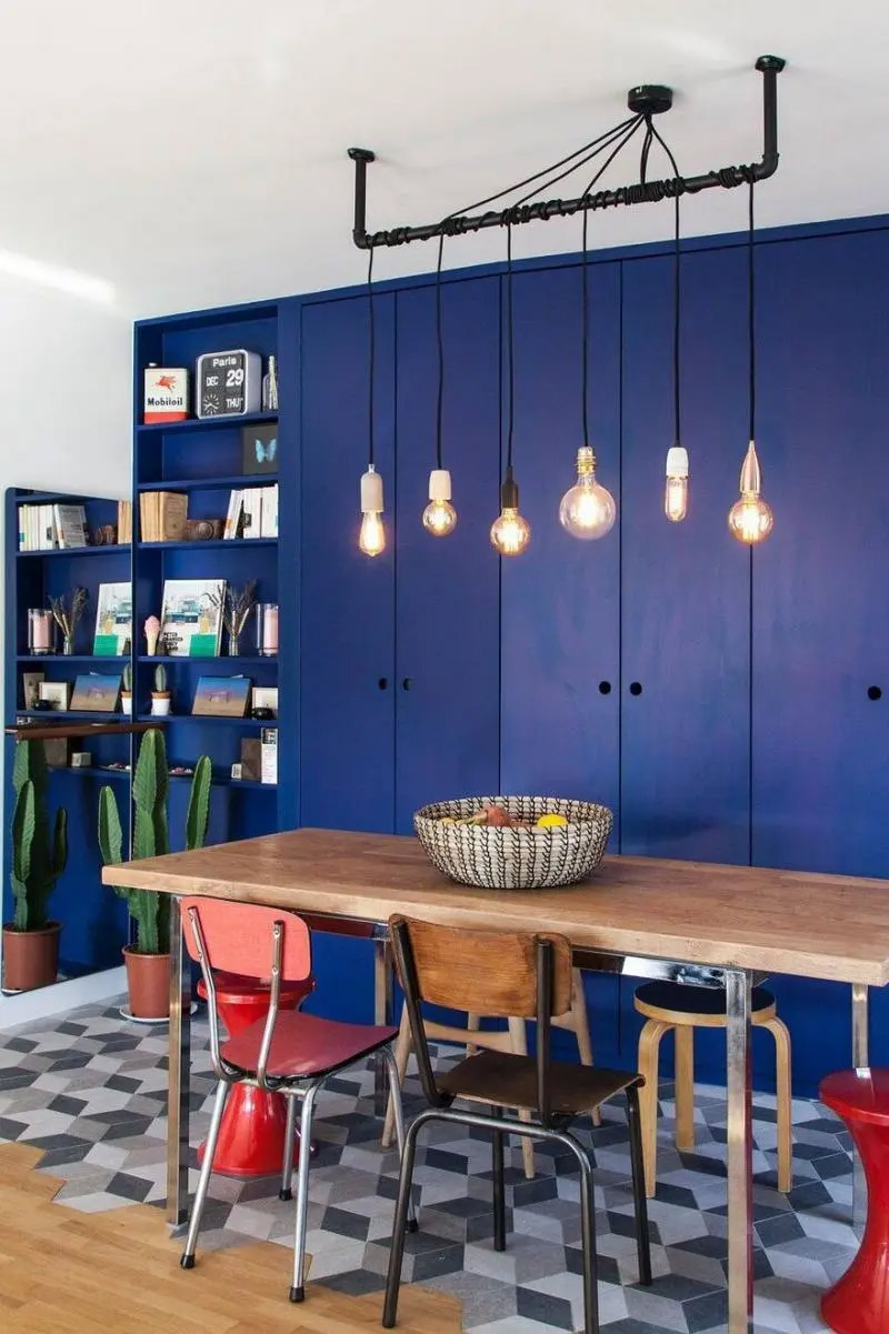 Une salle à manger brocante moderne aux placards bleu roi et ses chaises dépareillées