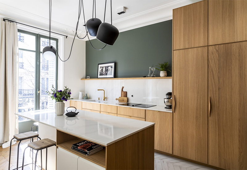 Une cuisine contemporaine dans un appartement haussmannien en bois avec un plan de travail et crédence blanc qui contraste avec un mur vert sapin