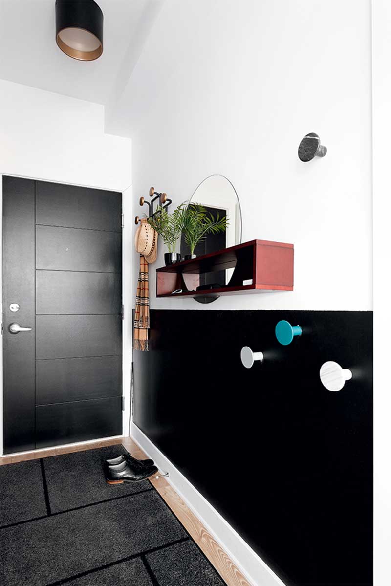 Entrée d'appartement moderne et design en noir et blanc avec une petite étagère murale et des patères de couleur
