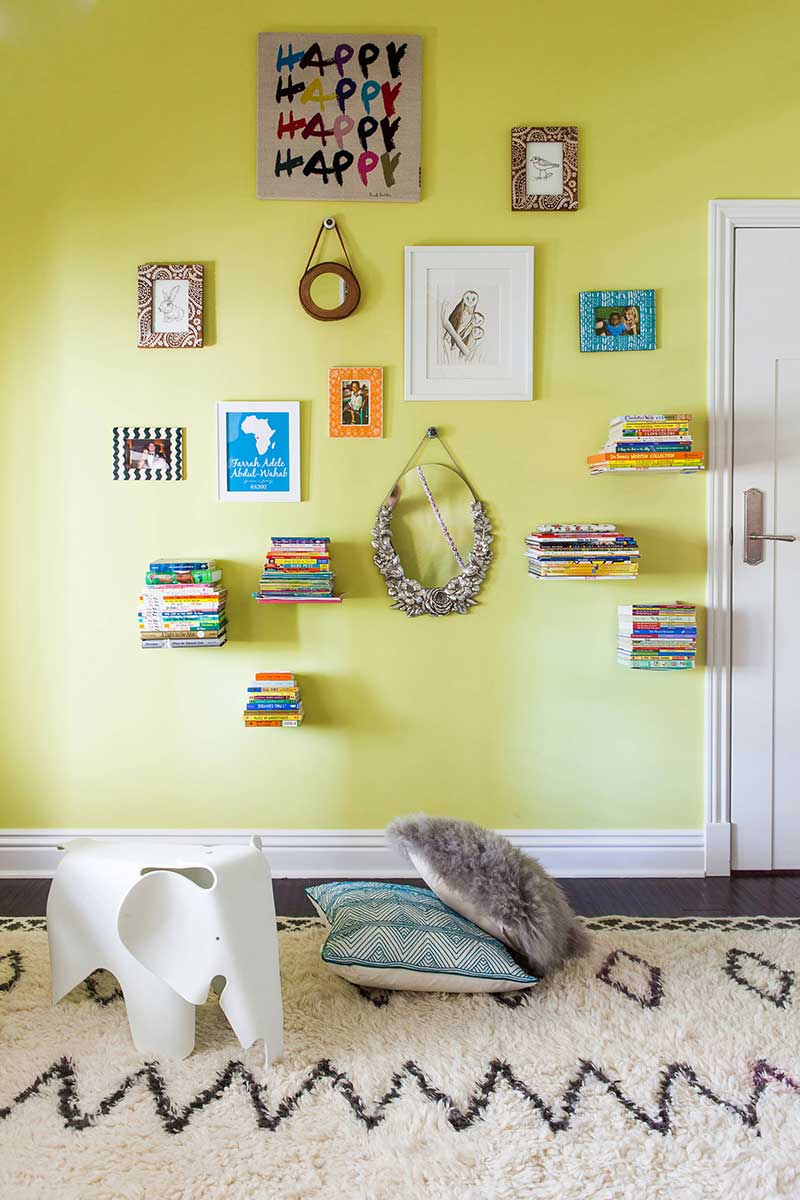 Un mur de chambre d'enfant jaune vif avec un mélange de petits cadres décos et d'étagères invisbles