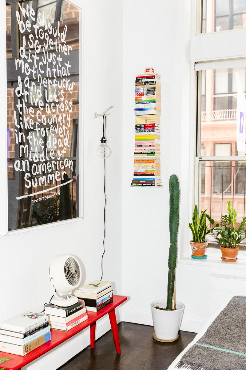 Étagère murale invisible de livres dans le studio de Timothy Goodman à New York entre plantes vertes et oeuvres d'art