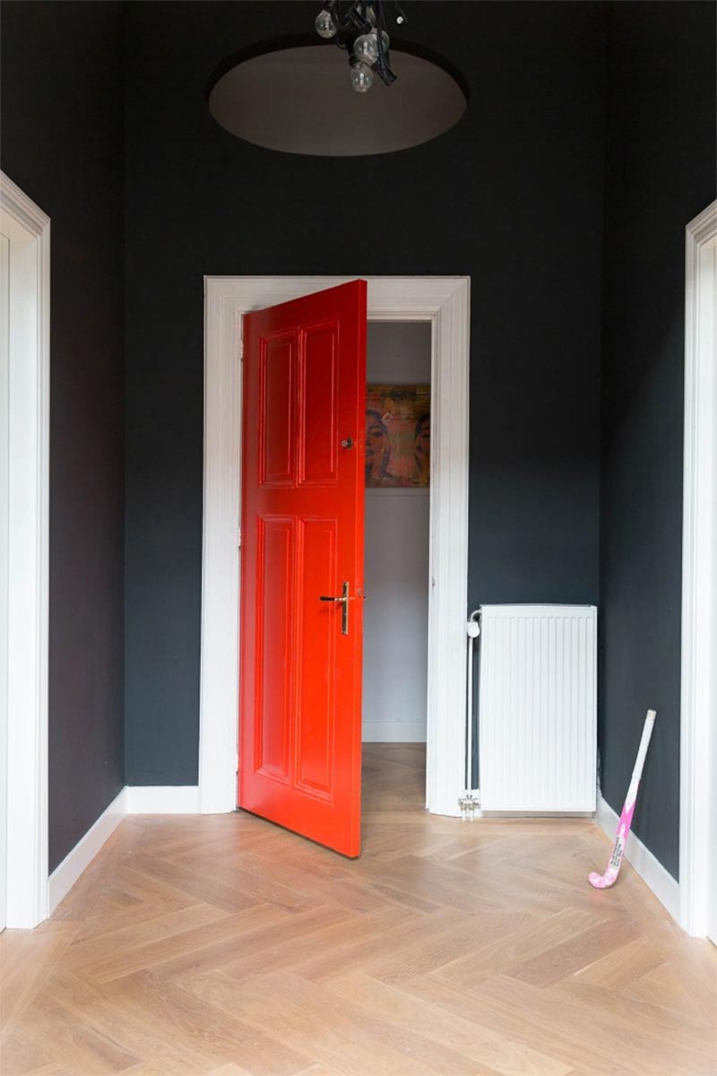Porte rouge, encadrement blanc et murs noir pour cette entrée