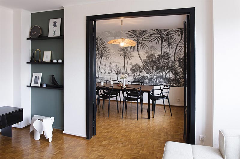 Un encadrement de porte peint en noir mettant en valeur la pièce adjacente et son papier peint panoramique