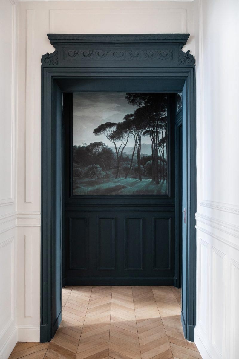 Un encadrement de porte ancien peint en bleu profond, faisant écho au papier peint du fond de couloir