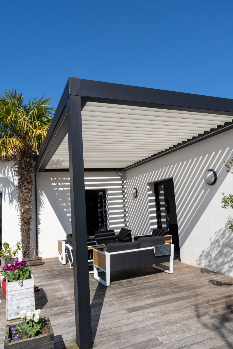 Une terrasse en bois protégée par une pergola bioclimatique en noir et blanc