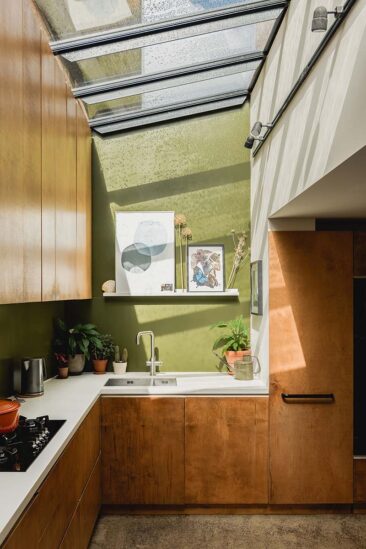 Une cuisine avec une fenêtre de toit, des meubles en bouleau teinté et un mur vert olive