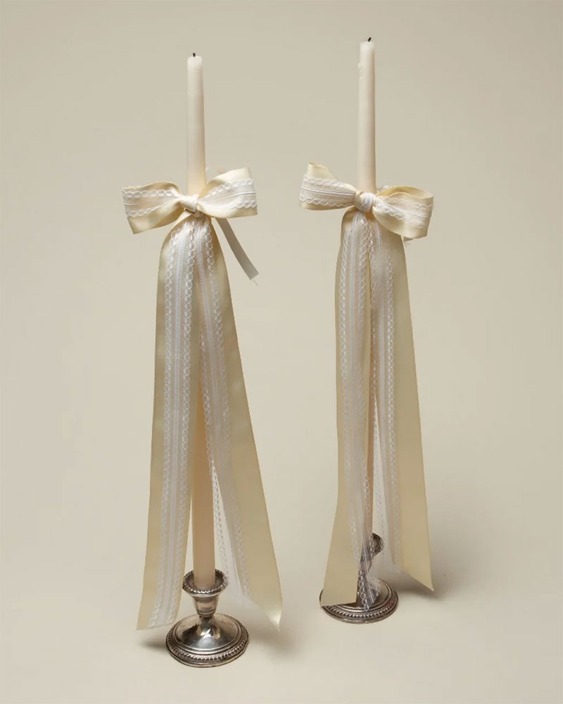 Bougeoirs anciens et longues bougies agrémentées de longs nœuds en satin blanc