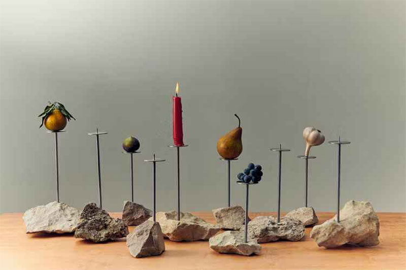 Des bougeoirs en métal planté dans des pierres, mettant en scène des fruits et une bougie