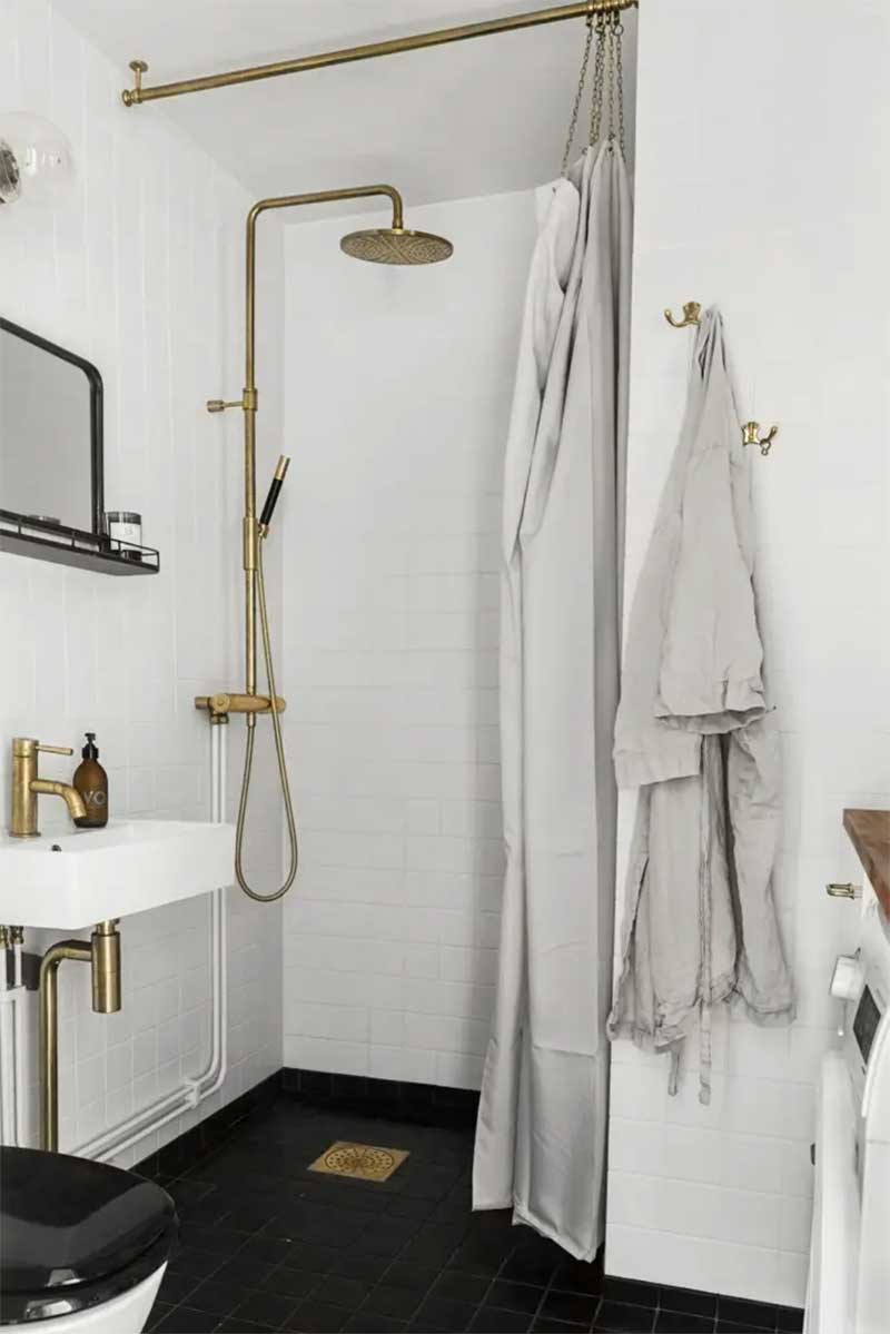 Une salle d'eau en noir et blanc adouci par un rideau de douche en lin et des détails en cuivre