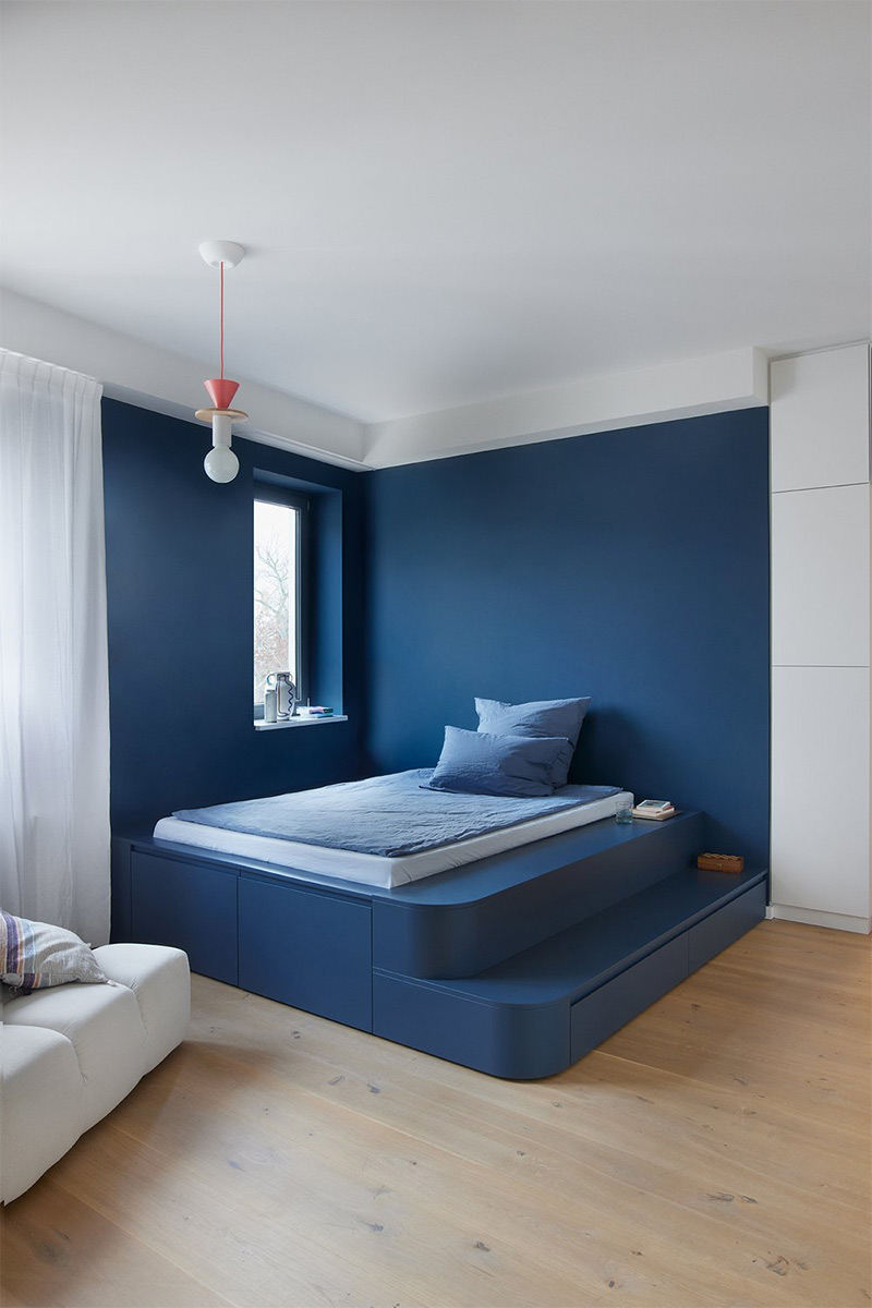 Un lit posé une plateforme et marqué par une couleur bleue pour une chambre blanche