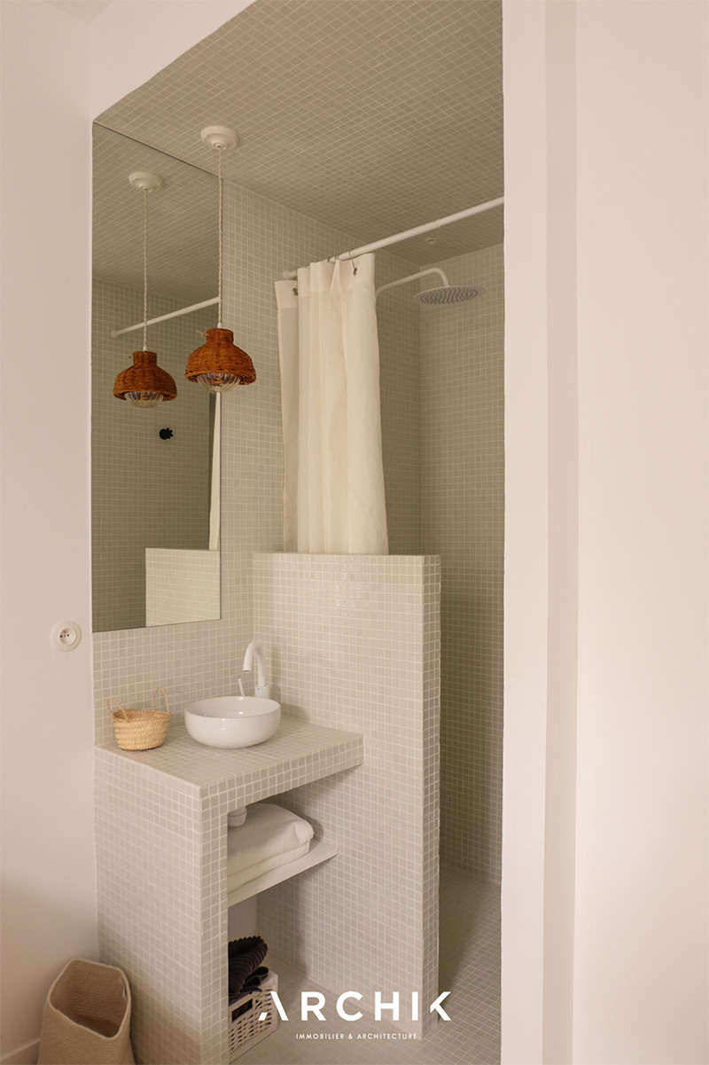 Une salle d'eau intégrée à la chambre, présentant une mosaïque de carreaux gris clair