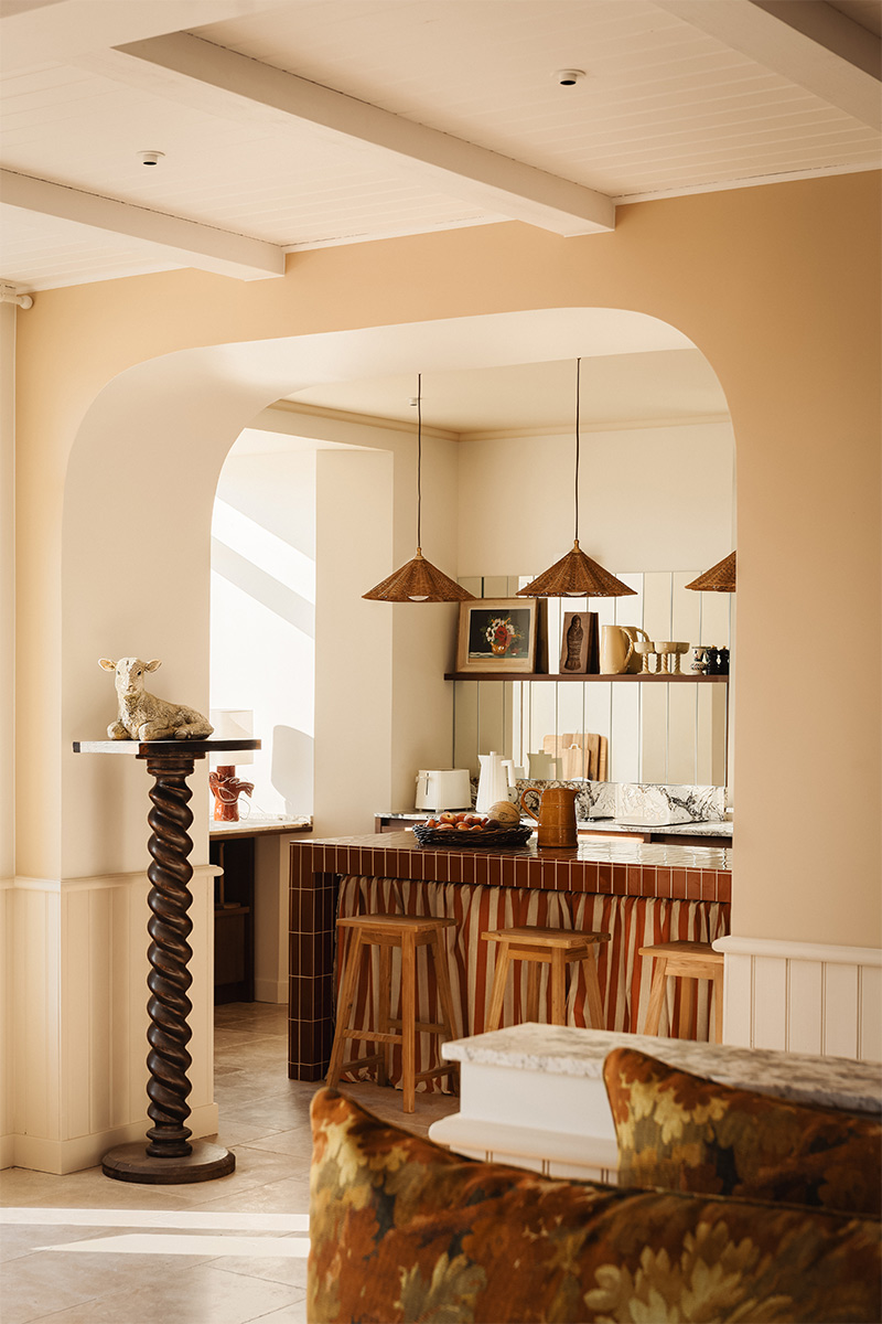 Vue sur l'espace cuisine et son îlot central réalisé en faïence rouge avec un rideau jupon aux rayures franches blanches et rouges