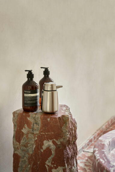 La douche avec son receveur en marbre rouge circulaire et son bloc surélévé pour poser les produits de beauté