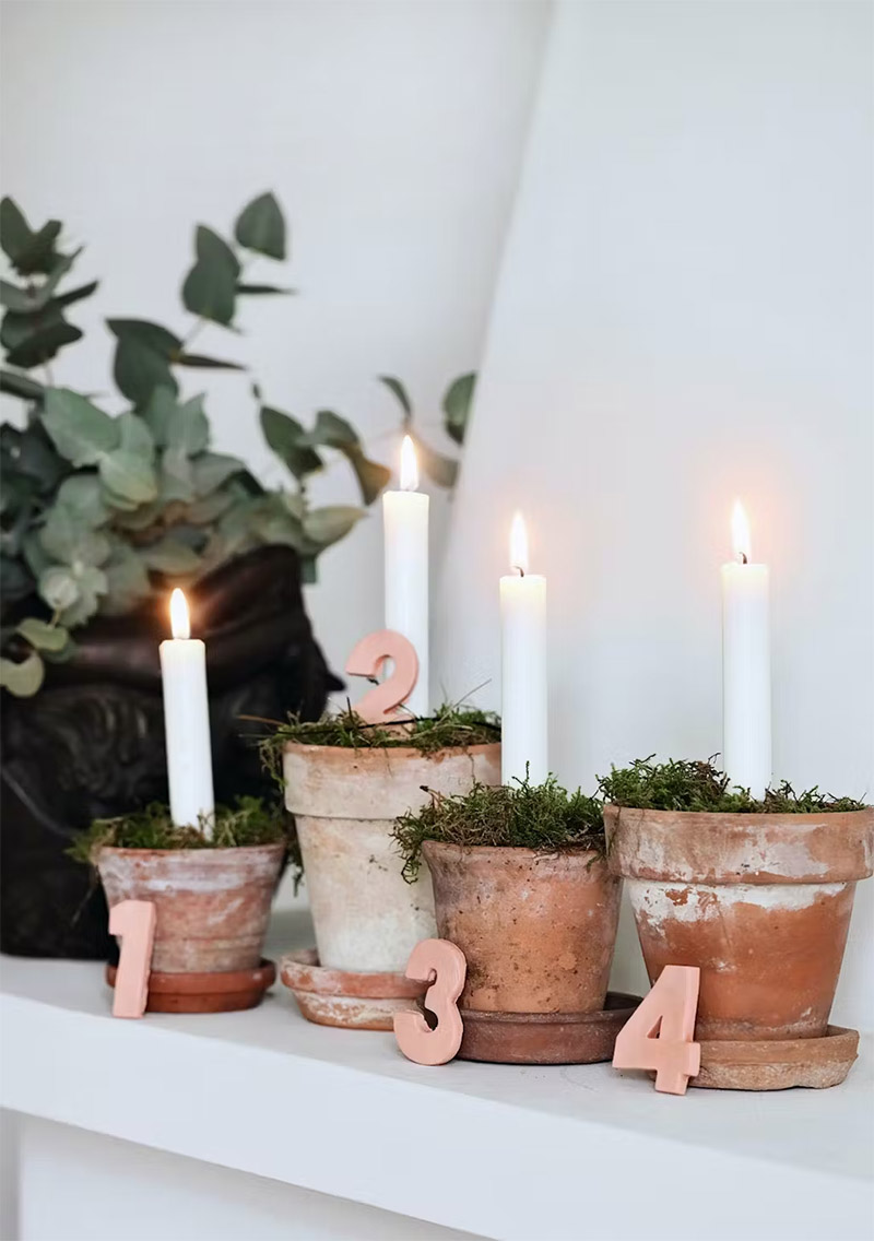 Pots de fleurs, mousse naturelle, bougies blanches et chiffres en bois pour un calendrier de l'avent décoratif