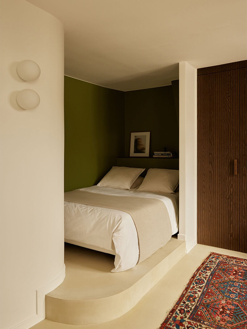 Un studio peint en blanc vanille avec un aplat de vert pour cadrer le coin lit