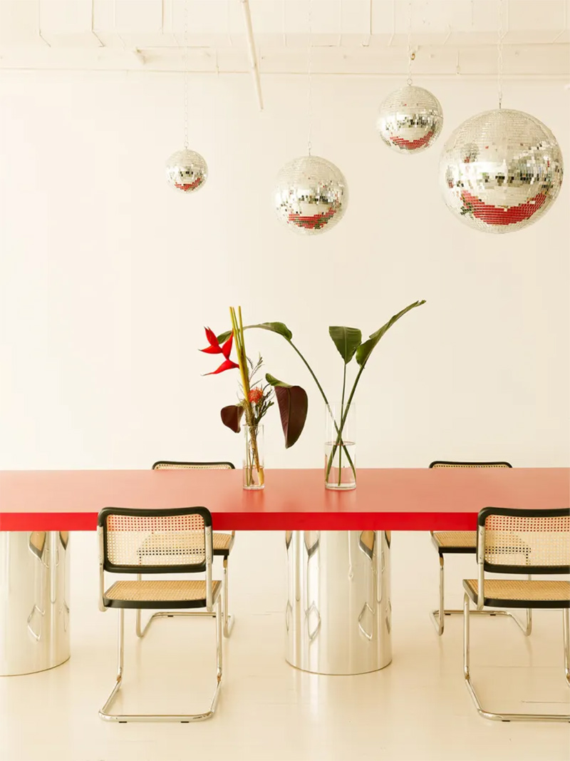 Table de repas aux pieds chromés et plateau rouge, avec en suspension des boules à facettes pour le fun