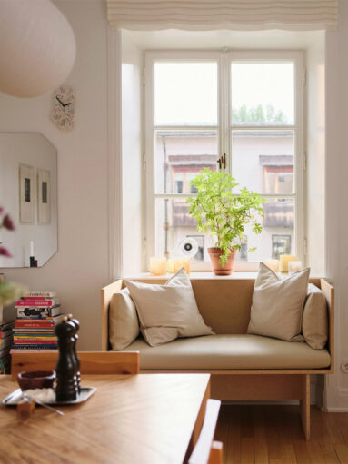 Banquette en bois coincée sous la fenêtre de la cuisine crée un coin cocooning avec ses coussins et son étagère de livres