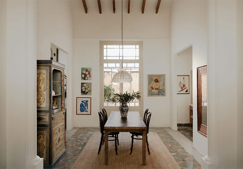 Une salle à manger à la décoration dépouillée des maisons de Méditerranée avec hauts plafonds poutres apparentes et sol ancien patiné